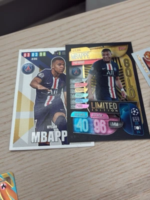 Fotbollssamlarkort Mbappé PSG - Två fotbollssamlarkort med Kylian Mbappé i PSG:s hemmaställ. Ett kort är Limited Edition med gulddetaljer och holografisk effekt, det andra har vita och guldiga inslag. Båda visar statistik och klubbmärke. Perfekt för samlare!