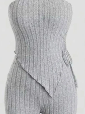 Grå ribbad topp med snörning - Säljer en snygg grå topp i ribbat material med snörning i sidan och asymmetrisk nederkant. Toppen är ärmlös och har en modern, edgy look som passar perfekt till jeans eller kjol. Perfekt för dig som vill sticka ut lite extra!