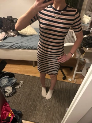 Randig ribbad klänning i rosa och svart - Kortärmad, kroppsnära klänning med ribbad struktur och horisontella ränder i svart, rosa och vitt. Klänningen har rund halsringning med svart kant och slutar strax ovanför knäna. Perfekt för dig som gillar en enkel men snygg look.