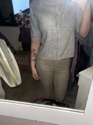 Grå kofta med pärlknappar lager 157 - Kort gråmelerad kofta från lager 157 med rund halsringning och pärlknappar framtill. Koftan har halvlånga ärmar och är stickad i ett mjukt material som känns skönt mot huden. Perfekt att slänga över en topp för en enkel men snygg look.