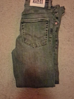 Blå jeans från Jack & Jones - Säljer ett par blå jeans från Jack & Jones med slitningar på benen och klassisk femficksdesign. Jeansen har en smal passform och är gjorda i denim med en snygg tvättad look. Perfekta för dig som gillar en avslappnad och trendig stil.