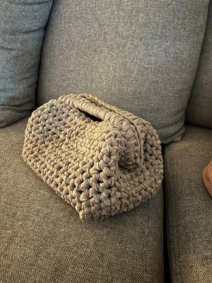 Virkad clutch bag - Unik handvirkad clutch bag i beige tjockt garn. Väskan har en rektangulär form med ett praktiskt handtag upptill, vilket ger en cool och trendig look. 27cm bred, 15cm hög.