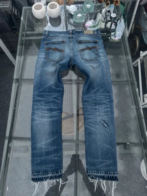 Nudie Jeans Lean Dean W30 L32 – slitna denim - Nudie Jeans Lean Dean i storlek W32 L30-32. Slim fit-modell med snygg wash och tydlig worn-in känsla.  ⚠️ Defekt: hål/slitage vid ena bakfickan (söm har gått upp, se bilder). Fransiga benslut samt mindre slitage på benet. Perfekt för dig som gillar vintage / raw denim look eller vill laga själv.  Pris satt efter skick.