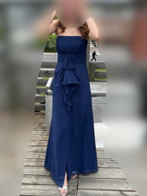 Balklänning  - Elegant marinblå långklänning med axelbandslös design och markerad midja. Klänningen har en dekorativ volang framtill och en lätt slits nedtill. Perfekt för bal eller festliga tillfällen.