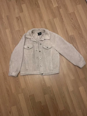Beige teddyjacka från soya - Mysig beige teddyjacka från Gina Tricot med två bröstfickor med lock och knappar framtill. Jackan har klassisk krage, sidofickor och är tillverkad i fluffigt teddy-material. Har rivits upp några cm på ena armen, inget man märker av för mycket.