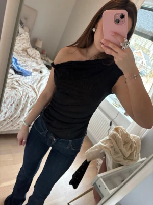 Svart oneshoulder body - Snygg svart oneshoulder topp med tight passform. Toppen har en draperad effekt över axeln och är ärmlös på ena sidan. Perfekt för dig som vill ha en stilren och trendig look.