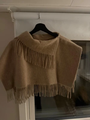 Beige ullsjal med fransar från E2 - Säljer en supermjuk och stilren beige sjal från malene birger. Sjalen är i ull och har snygga fransar längs kanterna samt en klassisk, rektangulär form. Perfekt att slänga över axlarna för en chill och trendig look. Ny och prislappen är kvar🫶🏻
