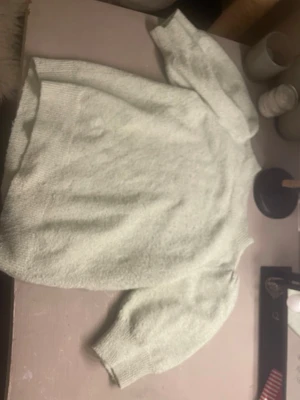 Ljusgrå stickad tröja med puffärm - Mysig ljusgrå stickad tröja med puffärmar och ribbade muddar vid ärmslut och nederkant. Tröjan har en avslappnad passform och är tillverkad i ett mjukt material som känns skönt mot huden. Perfekt för kyliga dagar.