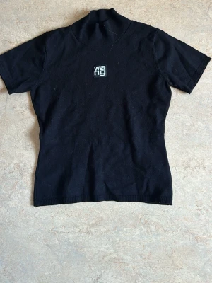  polotopp Alexander Wang - Säljer en svart polotopp från Alexander Wang med korta ärmar och broderad logga framtill. Toppen har en slim passform och är tillverkad i mjukt stickat material som sitter snyggt på kroppen. Den sitter tight och är mjuk. Inte äkta kompis men den ser ut att vara det. Passar XS-S