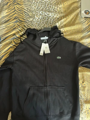 Svart Lacoste med dragkedja - Svart hoodie från Lacoste med dragkedja framtill och klassisk krokodillogga på bröstet. HELT NY OANVÄND, KOM MED BUD
