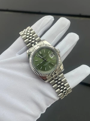 Seiko Datejust Mod - Specifikationer: Storlek: 39mm Urverk: Nh35 (Automatiskt) Material: 904L Rostfritt Stål Glas: Sapphire Glas Tavla: Grön/Olive Bezel: Räfflad Armband: Viklås och Justerbart  Krona: Screw Down Vattentålighet: 30 Meter Klocklåda ingår 