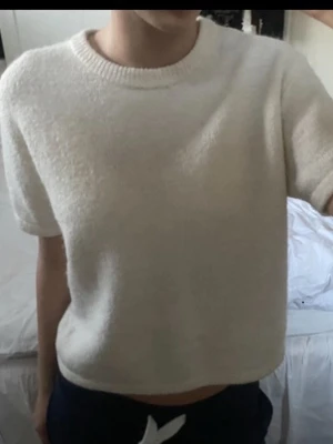 Vit croppad topp med kort ärm - Mysig vit croppad topp med korta ärmar och rund hals. Tillverkad i ett mjukt, fluffigt material som ger en avslappnad vibe. Perfekt att styla med höga jeans eller kjol för en enkel men trendig look.