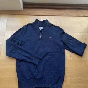 Morris half zip - Säljer en stilren mörkblå tröja från Morris med dragkedja och ett litet broderat emblem på bröstet. Tröjan har långa ärmar och ribbade muddar vid ärmslut och nederkant. Perfekt för en elegant och avslappnad look.