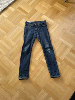 Mörkblå skinny jeans från Levi's - Säljer ett par mörkblå skinny jeans från Levi's med klassisk femficksdesign och lätt slitna detaljer vid knäna. Jeansen har normal midja, dragkedja och knapp framtill samt Levi's ikoniska läderpatch bak. Perfekta för en avslappnad och trendig look.