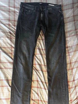 Mörkgrå jeans från Replay - Säljer ett par mörkgrå jeans från Replay med klassisk femficksmodell och raka ben. Jeansen har subtila slitningar och Replay-logga på myntfickan. Perfekta för dig som gillar en clean och stilren look.