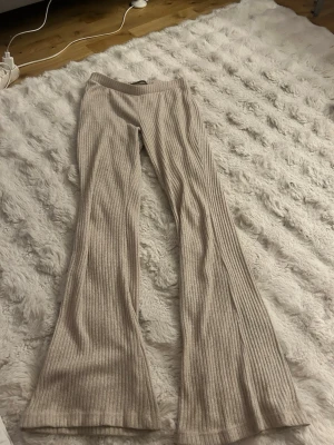 Beige ribbade bootcut leggings - Säljer ett par beige ribbade leggings med bootcut-modell. De har hög midja och är tillverkade i ett mjukt, stretchigt material som sitter skönt på kroppen. Perfekta för en avslappnad och trendig look.