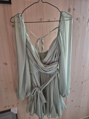 Ljusgrön jumpsuit med volang - Supersöt ljusgrön jumpsuit med omlott och volangdetaljer. Den har långa, luftiga ärmar som är öppna, knyt i midjan och öppen rygg med snörning. Perfekt för sommarens alla tillfällen!