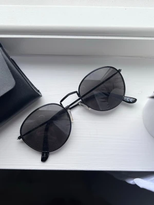 Svarta runda solglasögon (mycket bra skick) - Ett par stilrena solglasögon med rund form och svarta metallbågar. Glasen är mörka, ger en cool look och minimalistisk stil. 