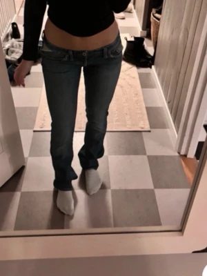Låga bootcut jeans i blå denim - Säljer ett par blå bootcut jeans med väldigt låg midja och klassisk femficksdesign. Jeansen har en snygg tvätt och sitter tajt över höfterna med utsvängda ben. Perfekta för en trendig och avslappnad look. Passar Xs-S
