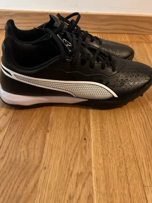 Svarta Puma fotbollsskor med dobbar - Säljer ett par svarta fotbollsskor från Puma med vita detaljer. . Skorna har snörning och små dobbar på sulan på konstgräs eller grus. .