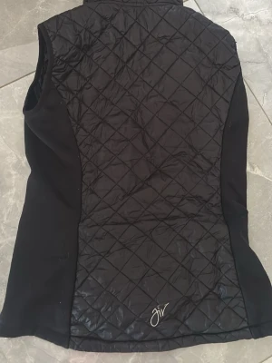 Svart kånatåkningsväst från karisma - Snygg svart väst från karisma. Bra för konståkningsträningar. Säljer då jag slutat. Svart rutigt mönster med fickor och loggan  insydd längst ner på ryggen. Nypris 1200