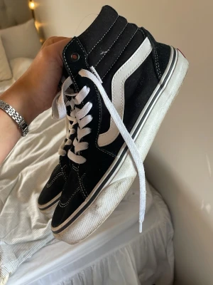Svarta Vans Sk8-Hi sneakers - Klassiska Vans Sk8-Hi sneakers i svart mocka och canvas med vit sula och vit ikonisk sidostripes. Skorna har vita snören och kontrastsömmar som ger en snygg retrostil. Perfekta för dig som gillar streetwear och skatekänsla. Andvända några få gånger och kommer tvättas innan köp 