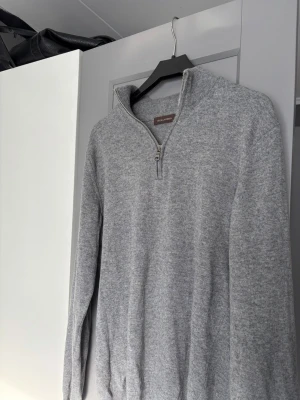 Grå halvzip tröja Oscar Jacobson - Snygg grå stickad tröja från Oscar Jacobson med halvzip och hög krage. Perfekt för lager på lager och enkel att matcha med olika outfits.