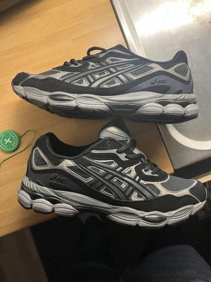 ASICS Gel-NYC svarta - passar 41-43 ASICS Gel-NYC sneakers i svart och grå mesh med detaljer i syntet och reflekterande material. Skorna har en chunky sula och klassisk ASICS-logga på sidan. Perfekta för dig som gillar retrovibbar och streetwear. Finns i flera färgkombinationer.