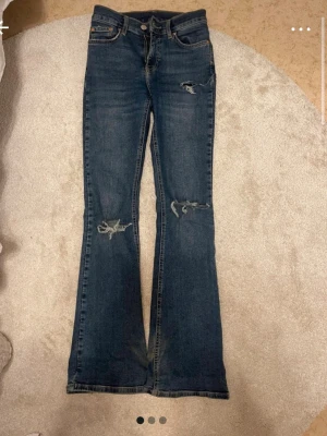 Mörkblå bootcut jeans med slitningar - Snygga mörkblå bootcut jeans med slitningar på knäna och låret. Jeansen har klassisk femficksdesign och låg midja. Perfekta för dig som gillar en avslappnad och trendig look.