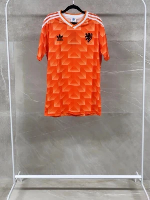 Retro fotbollströja Adidas - Säljer en orange retro fotbollströja från Adidas med geometriskt mönster, vita ränder på axlarna och svart logga samt lejonmärke på bröstet. Perfekt för dig som gillar klassisk sportstil och vill sticka ut på planen.  Finns i olika storlekar!!! Pris kan diskuteras!!!