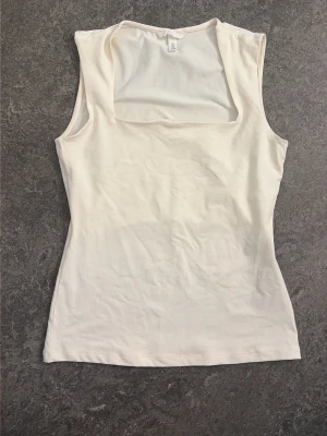 Vit ärmlös linnetopp - Snygg vit linnetopp med breda axelband och fyrkantig ringning. Toppen är enkel och stilren, perfekt att matcha med jeans eller kjol. Tillverkad i mjukt material som känns skönt mot huden.