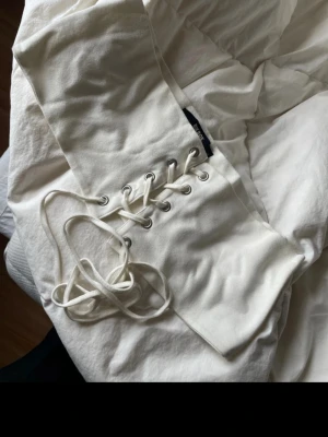 Vit snörad topp från BikBok - Snygg vit topp från BikBok i bomull med cool snörningsdetalj framtill. Perfekt att styla med jeans eller kjol för en trendig look. Toppens material känns mjukt och bekvämt mot huden.