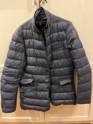 Massimo Dutti dunjacka - Säljer en snygg quiltad dunjacka från Massimo Dutti i mörkblå färg. Modellen är en elegant hybrid mellan kavaj och dunjacka vilket gör den perfekt både till vardags och mer uppklätt.  Knapparna samt dragkedjehänget är utbytta men fungerar perfekt och påverkar inte funktionen.