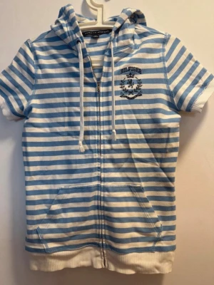 Blåvit randig hoodie Tommy Hilfiger - PRIS KAN DISKUTERAS!!!Säljer en blåvit randig hoodie från Tommy Hilfiger med dragkedja, korta ärmar och fickor framtill. Huvan har vita snören och på bröstet finns ett tryckt Hilfiger-emblem. Perfekt för en avslappnad och sportig stil.