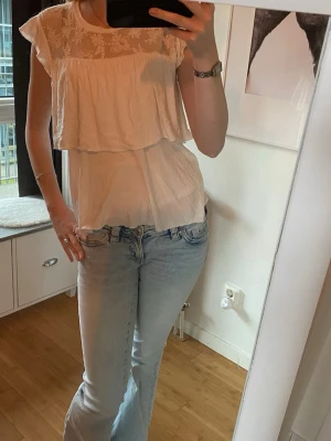 Vit blus med spetsdetaljer - Söt vit blus med spets upptill och volang över bysten. Använd få gånger, en liten fläck på ryggen men inget märkvärdigt. I storlek 170 men sitter som S