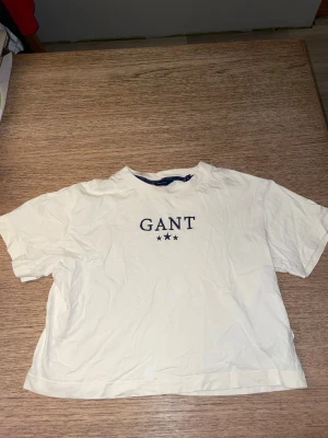 Vit kortärmad t-shirt från GANT - Säljer en vit t-shirt från GANT med klassisk logga och tre stjärnor tryckta framtill. T-shirten har en depth rund halsringning och är kortärmad. Tillverkad i mjuk bomull och har en relaxed, lite sensitive passform.