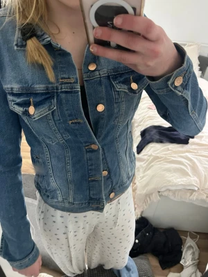 Klassisk blå jeansjacka - Snygg blå jeansjacka med guldiga knappar och två bröstfickor med lock. Figurnära passform och klassisk krage. Perfekt att slänga över en hoodie eller t-shirt för en cool och avslappnad look.