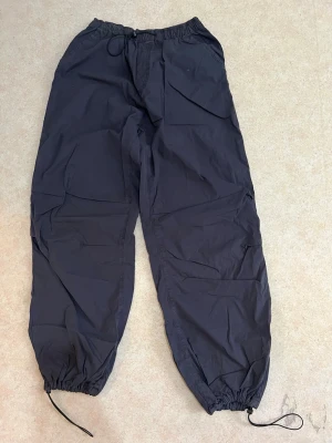 Mörkgråa Parachute pants - Byxorna har en lös passform och är tillverkade i ett vindtätt och vattenavvisande material, perfekta för kalla dagar utomhus. Den är använd kanske 2 gånger max. 