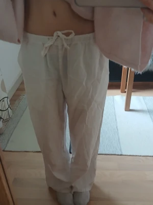 Vita linnebyxor med dragsko - Säljer ett par vita linnebyxor med avslappnad passform och dragsko i midjan. Byxorna har raka ben och är tillverkade i ett tunt, luftigt linnematerial som passar perfekt för en chill och stilren look.