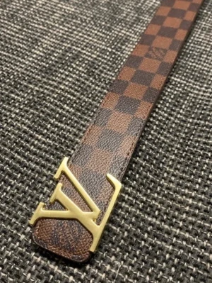  brunt rutigt bälte - Säljer ett ikoniskt  bälte med klassiskt brunt rutigt mönster i guld. Bältet är gjort i skinn och har en exklusiv känsla som lyfter vilken outfit som helst.