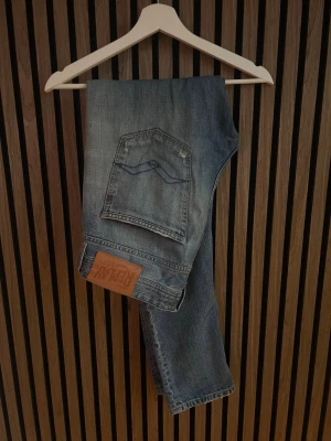 Replay jeans willbi - Säljer ett par blå jeans från Replay med snygga slitningar på låren och klassisk femficksmodell. Jeansen har en rak passform och detaljerad bakficka med Replay-lapp i läder. Perfekta för en avslappnad och trendig stil.