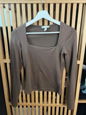 Brun långärmad topp - Snygg brun långärmad topp hm med en modern fyrkantig ringning. Tillverkad i mjuk bomull som känns skön mot huden. Perfekt att styla med jeans eller kjol för en clean look.