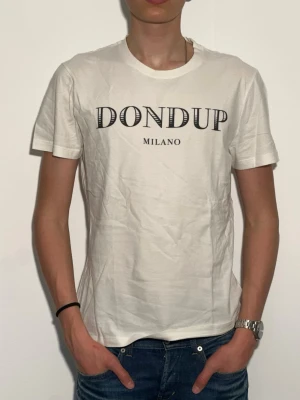 Vit Dondup Milano t-shirt - Snygg vit t-shirt från Dondup med svart text 'DONDUP MILANO' på bröstet. Klassisk rund halsringning och korta ärmar. Perfekt till jeans för en clean och stilren look.