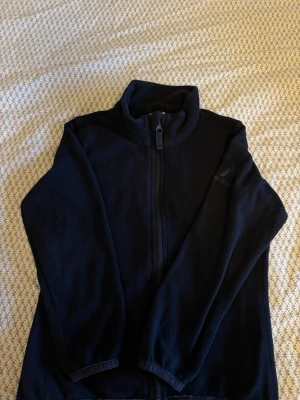 Mörkblå fleecejacka från McKinley - Mysig mörkblå fleecejacka från McKinley med hel dragkedja och hög krage. Perfekt för lager-på-lager och håller dig varm under kyliga dagar. Tillverkad i mjukt fleecematerial som känns skönt mot huden.