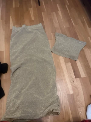 Glittrigt guldigt set med kjol och topp - Säljer ett glittrigt set i guld med en lång, åtsittande kjol och matchande tubtopp. Materialet är stretchigt och skimrar snyggt i ljuset, perfekt för dig som vill sticka ut. Settet är från Gina tricot  ge gärna ett prisförslag 🫶🏻