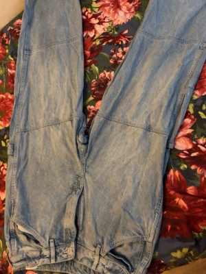 Ljusblå baggy jeans med sömdetaljer - Säljer ett par ljusblå baggy jeans med raka ben och markerade sömmar över knäna. Jeansen har stora bakfickor och bälteshällor. Perfekta för en avslappnad och trendig stil. Materialet är klassisk denim i bomull.
