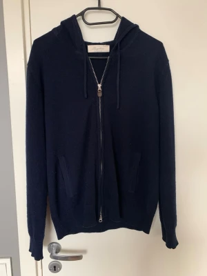 Mörkblå zip hoddie från Sayless - Mysig mörkblå hoodie från Say less  i kashmir med huva, snörning och hel dragkedja framtill. Två fickor på sidorna och ribbade muddar vid ärmslut och nederkant. Perfekt för en chill och stilren look. Nu ska denna tröja tyvärr säljas pga för liten men den är så sjukt skön och snygg.