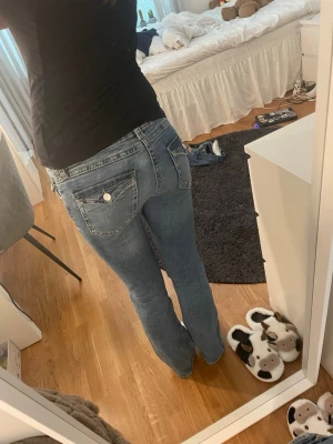 Blå bootcut jeans med fickdetaljer - Säljer ett par blå bootcut jeans med snygga fickdetaljer och silverknappar bak. Jeansen har klassisk femficksdesign och är tillverkade i ett mjukt denimtyg med lätt tvättad look. Perfekta för dig som gillar en avslappnad men trendig stil.