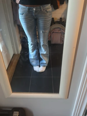 Ljusblå bootcut jeans med slitningar ifrån Gina tricot  - Säljer ett par ljusblå bootcut jeans med slitningar på knäna och klassiska fem fickor. Jeansen har låg midja.