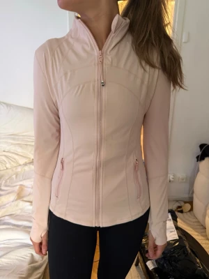 Ljusrosa träningsjacka Lululemon - Saljer nu min fantastiska Lululemon Define Jacket i en mjuk och fräsch ljusrosa nyans. Denna säljs ej längre och är väldigt svår att få tag på. Nypris: 1380kr. Detta är den ikoniska jackan som blivit viral som "BBL-jacket" tack vare de strategiska sömmarna som ger en otroligt smickrande och "snatched" siluett. Jackan är gjord i ett mjukt, stretchigt material som ger både stöd och full rörelsefrihet. Den är perfekt som lager-pa-lager plagg till gymmet, på löpturen